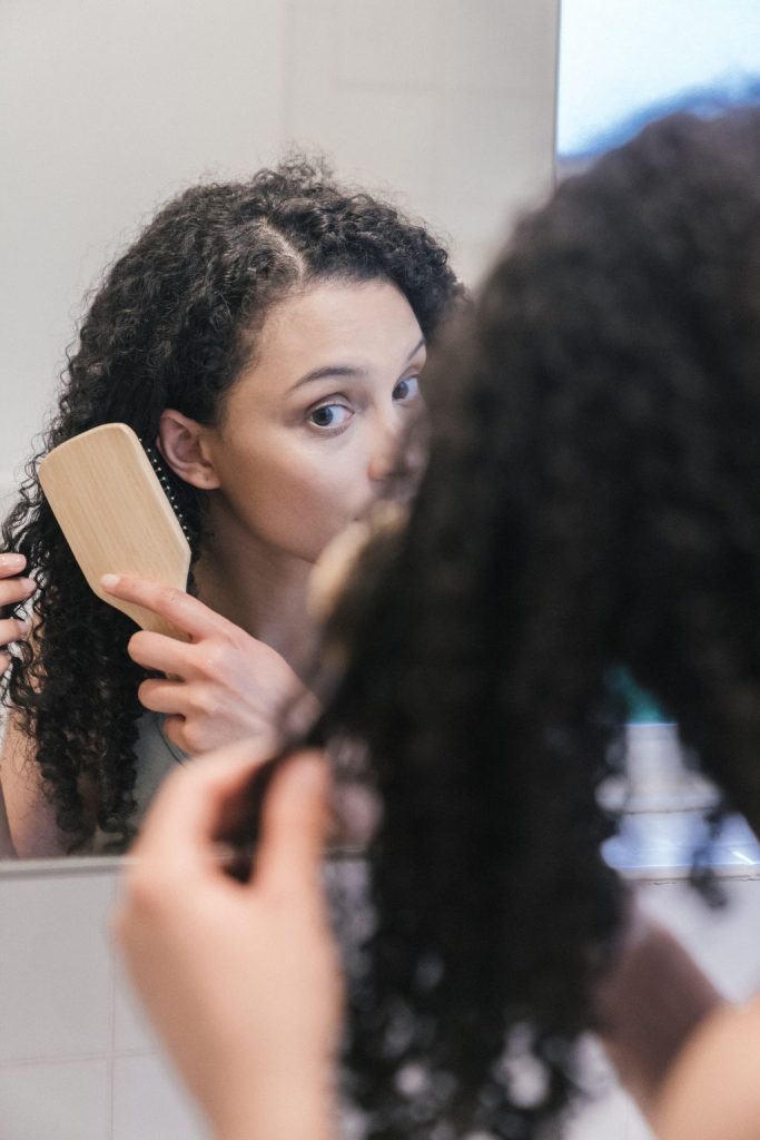 Femme aux cheveux bouclés se brossant les cheveux devant un miroir