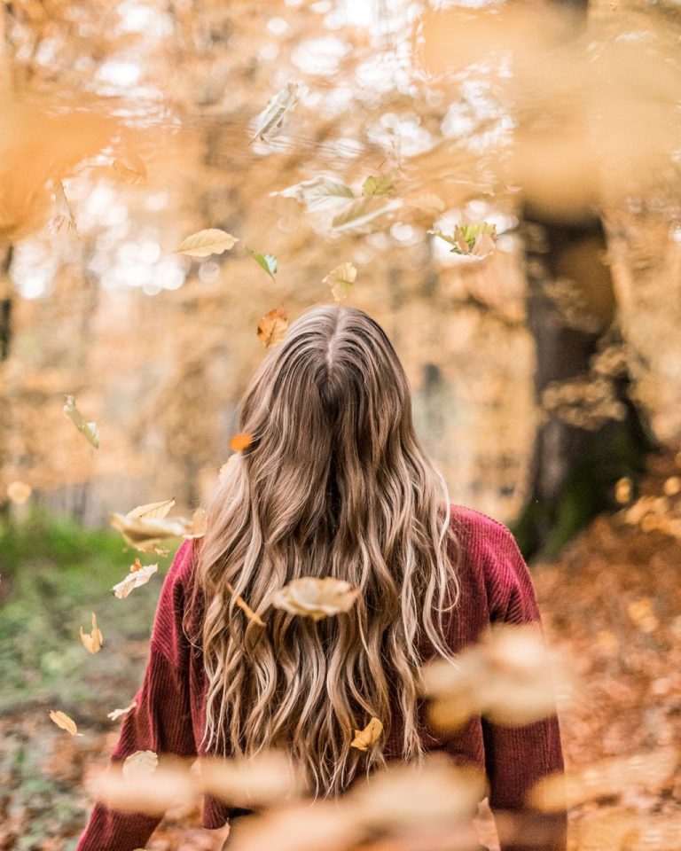 Femme de dos aux cheveux longs entourée de feuilles d'automne